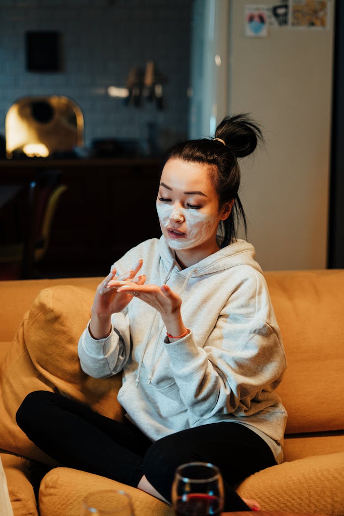 Asian woman enjoying a skincare routine at home while relaxing on a couch.