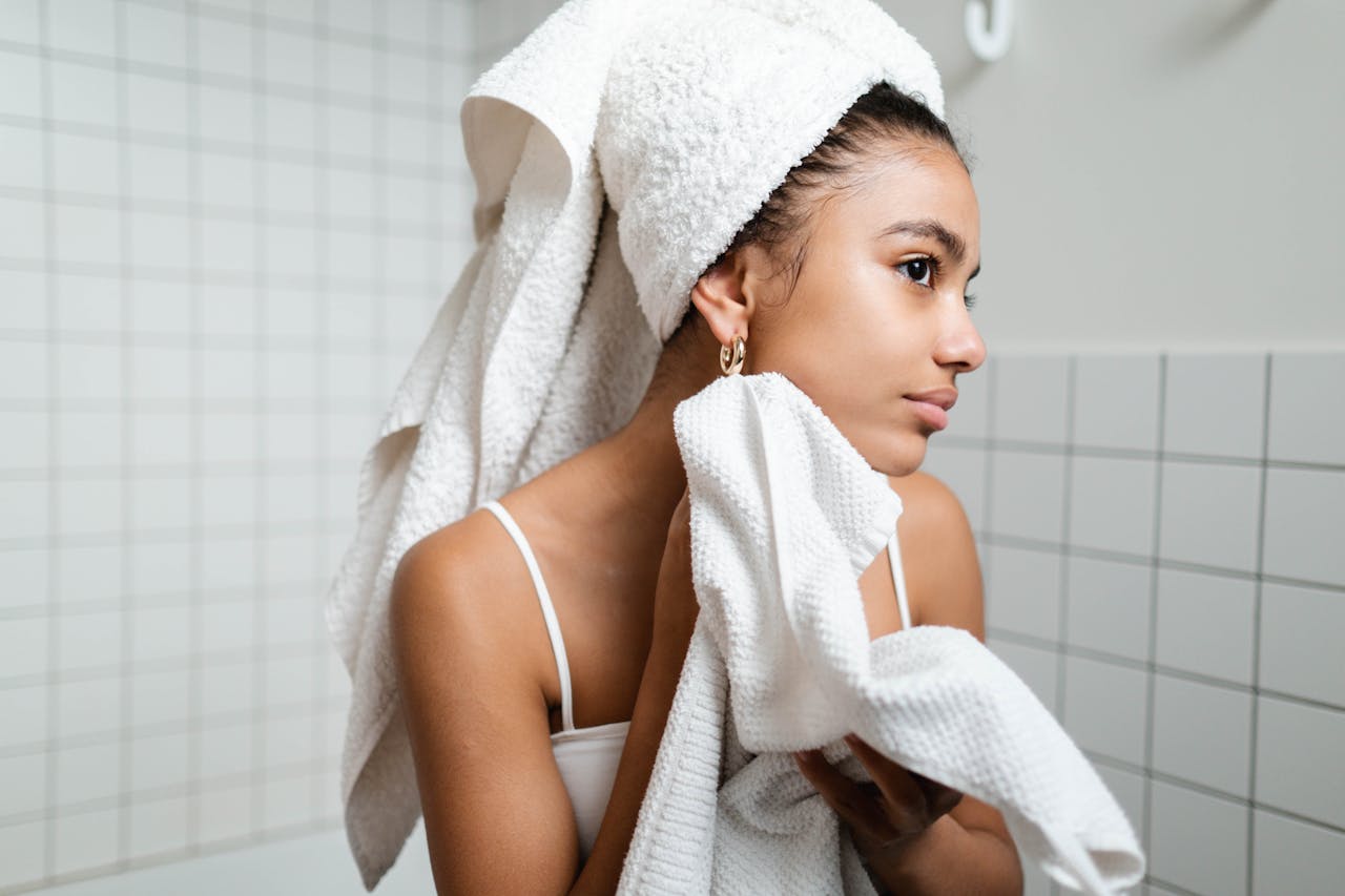 Young woman drying face with towel during morning skincare routine in a modern bathroom.